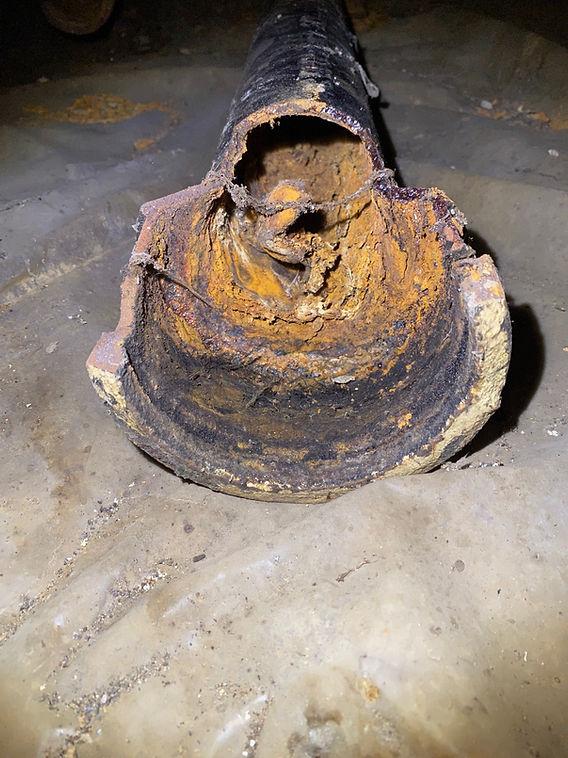 A corroded, rusted cast iron drain pipe in an old basement