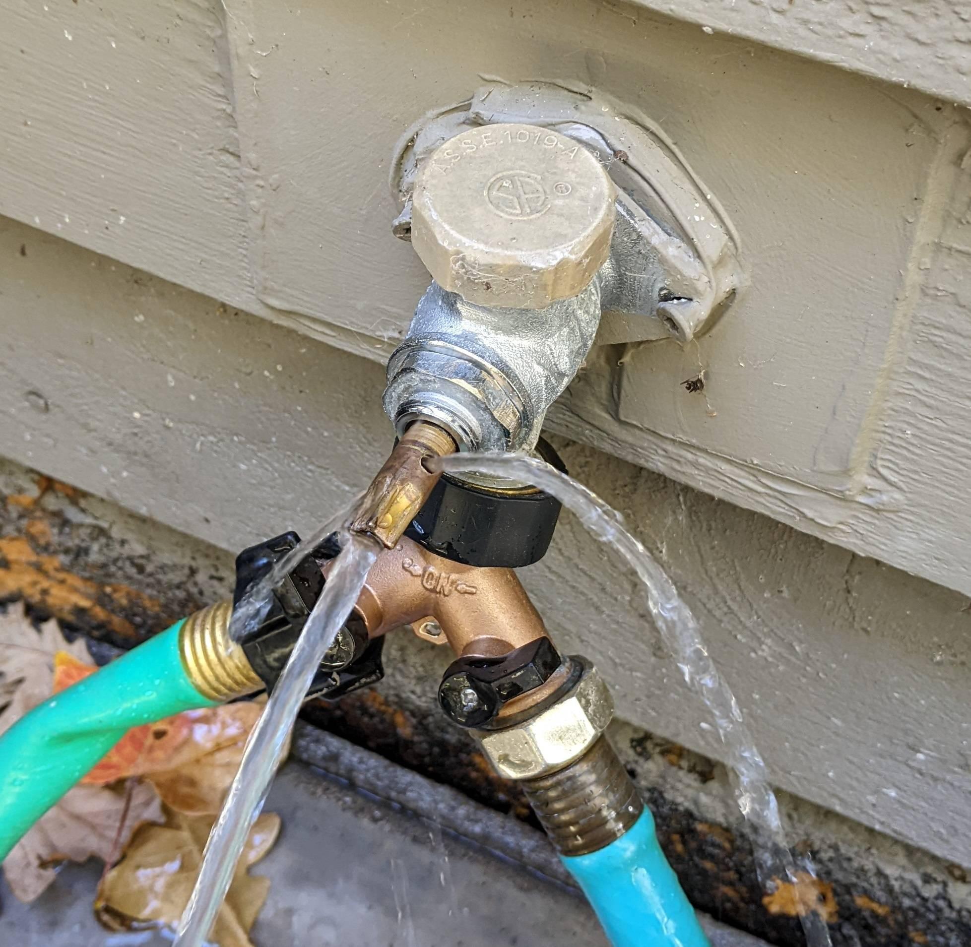 A frozen outdoor faucet and garden hose covered in ice in winter