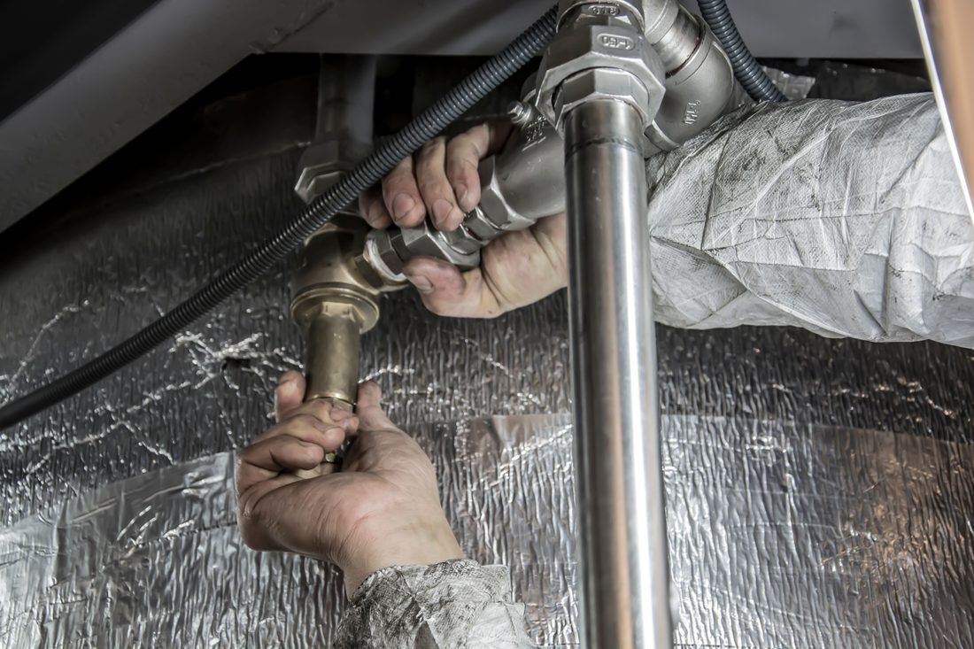 Hands servicing pipes under a sink